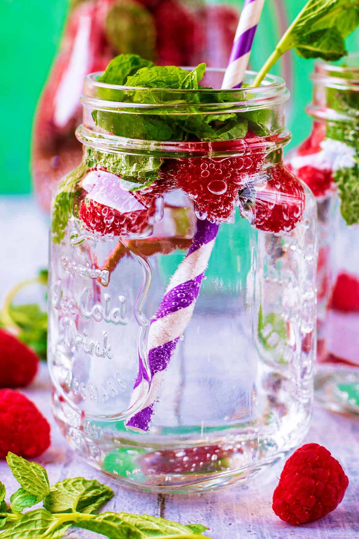 A mason jar filled with raspberry sparkling water with a striped straw.