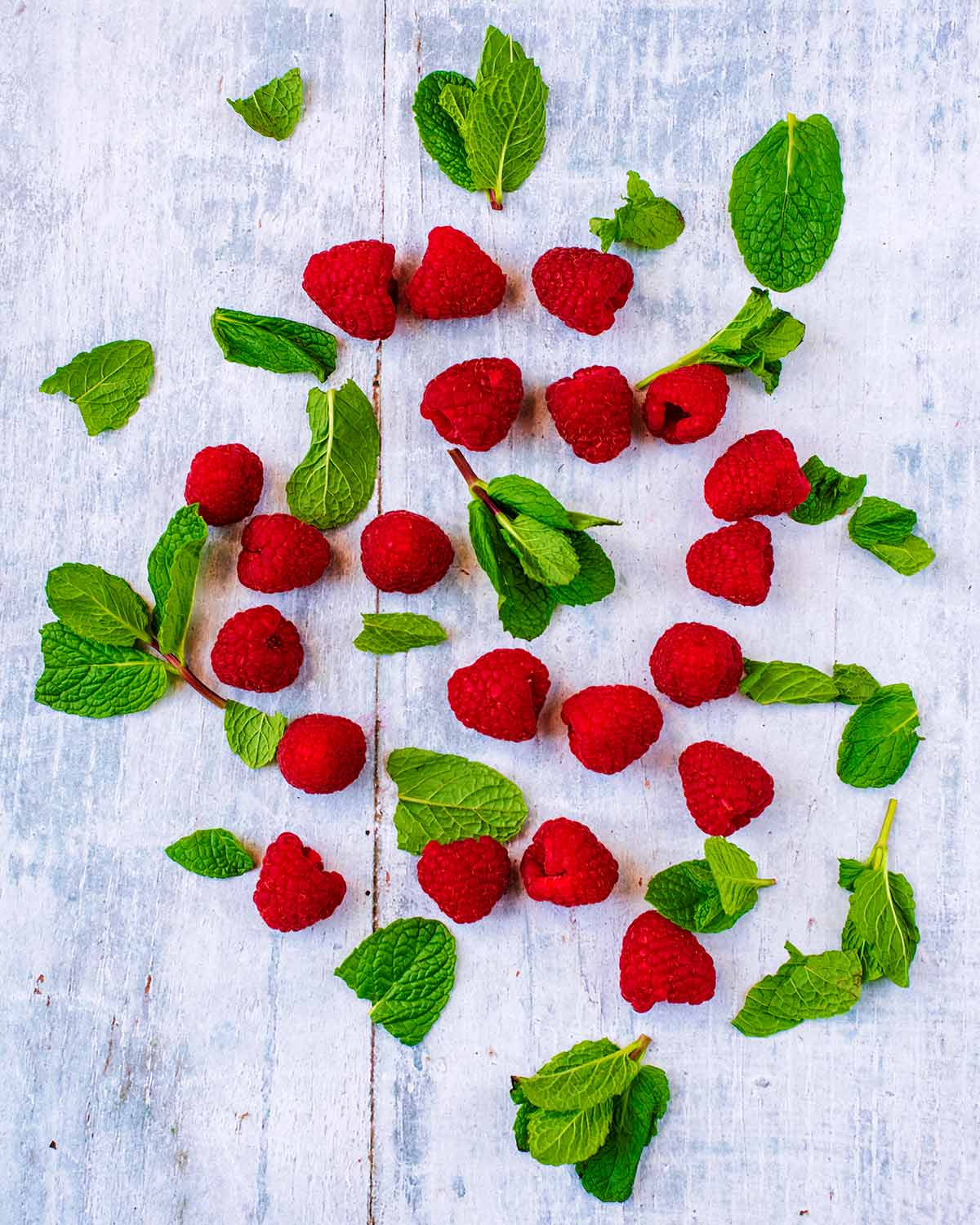 Fresh raspberries and mint leaves scattered over a grey wooden surface.