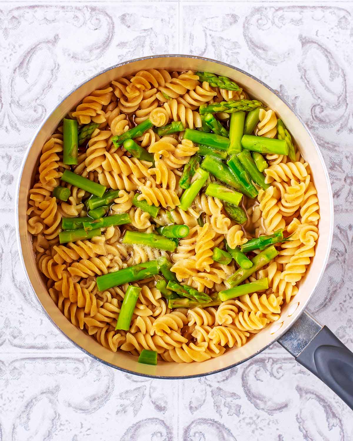 A saucepan containing cooked fusilli pasta and asparagus.