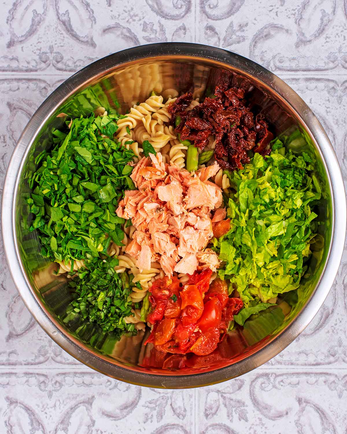 A large metal bowl containing cooked pasta, lettuce, tomatoes and asparagus.