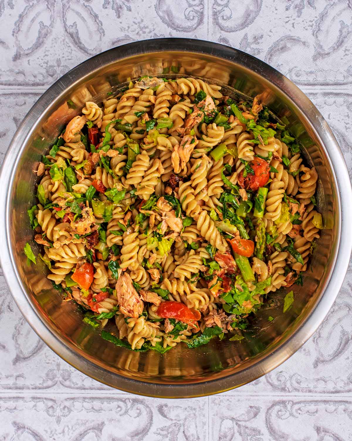 A large metal bowl containing a mixed salmon pasta salad.