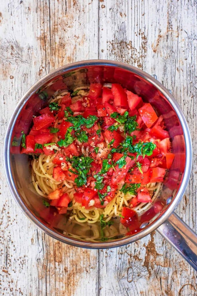 A saucepan containing cooked spaghetti, chopped tomatoes, chopped basil and crushed garlic.