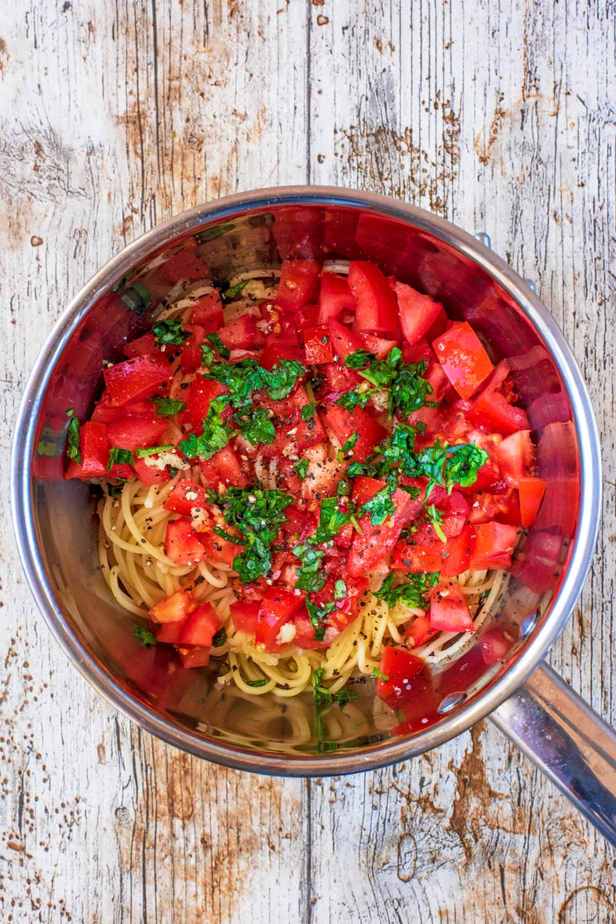 A saucepan containing cooked spaghetti, chopped tomatoes, chopped basil and crushed garlic.