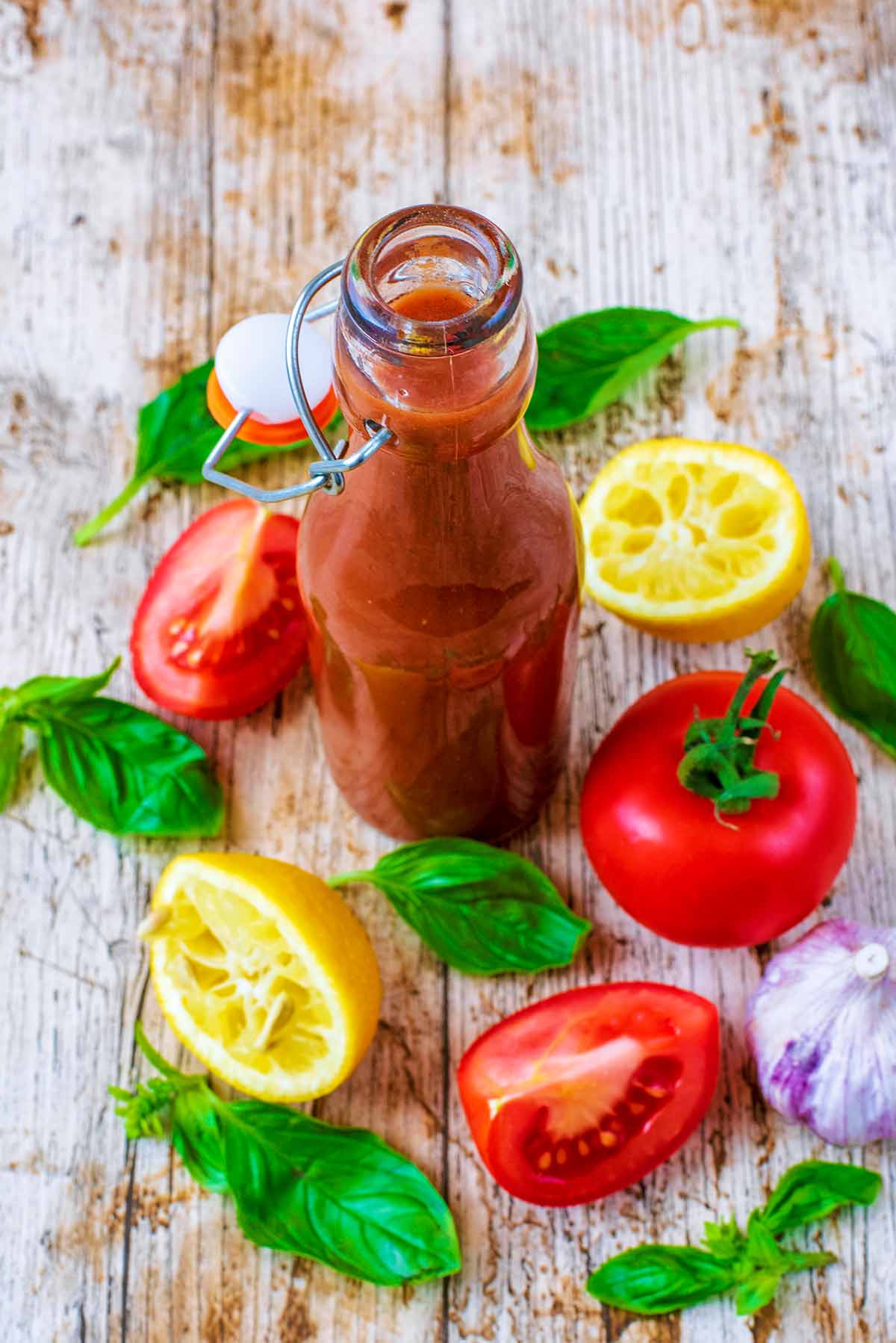 A bottle of Tomato Vinaigrette next to a tomato, lemon halves and basil leaves.