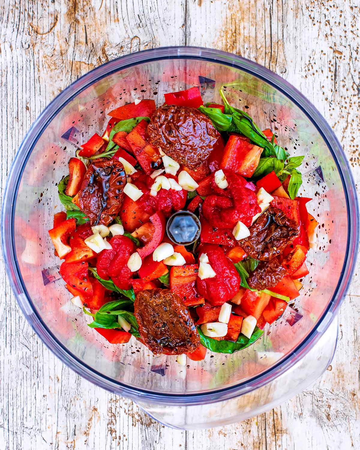 A food processor containing toatoes, chopped red pepper, crushed garlic and basil leaves.