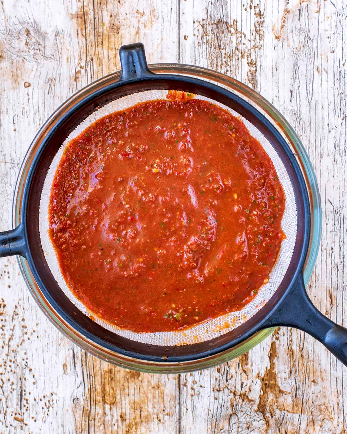 Tomato vinaigrette being sieved into a glass bowl.