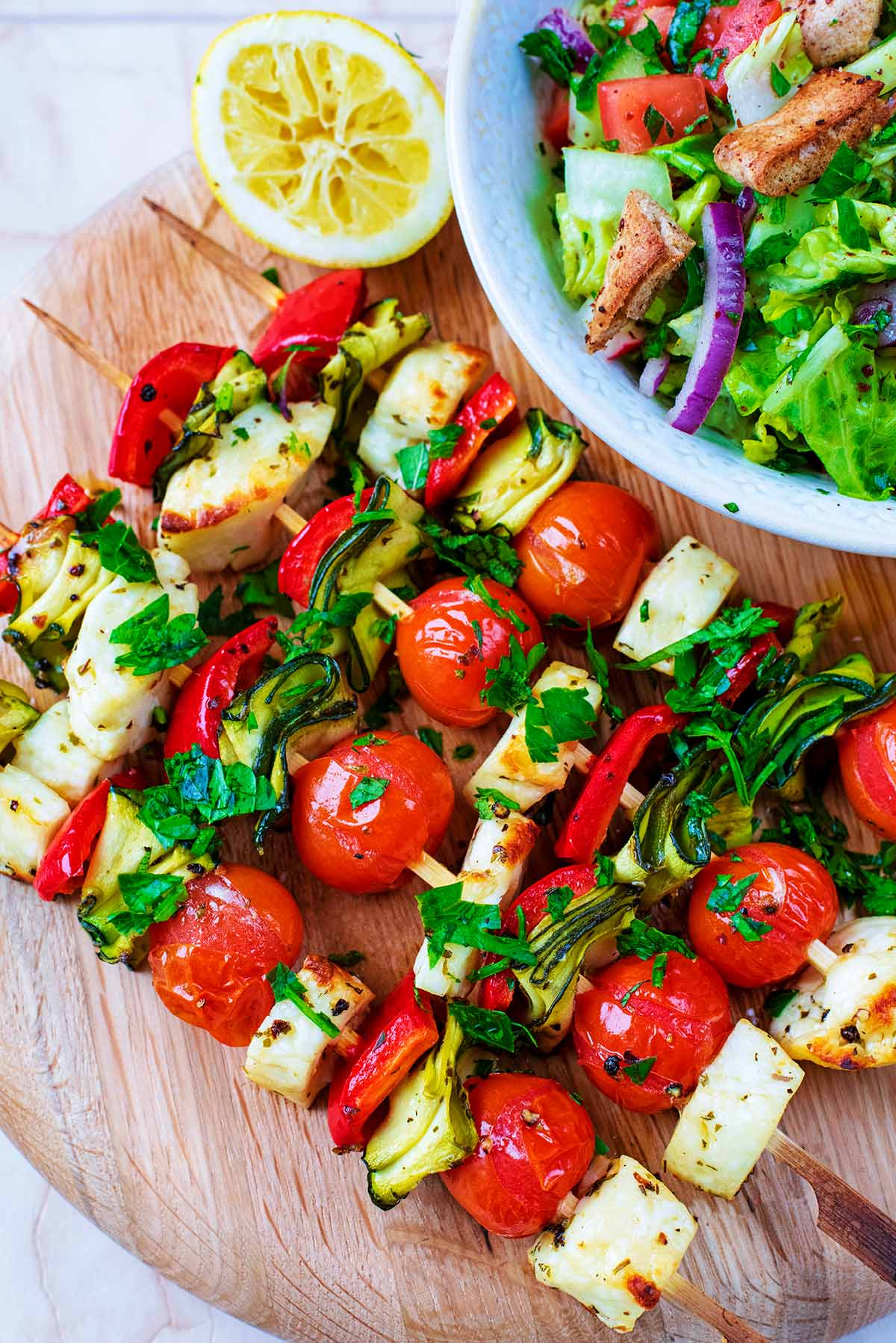 Vegetables and halloumi cubes on skewers next to a bowl of salad.