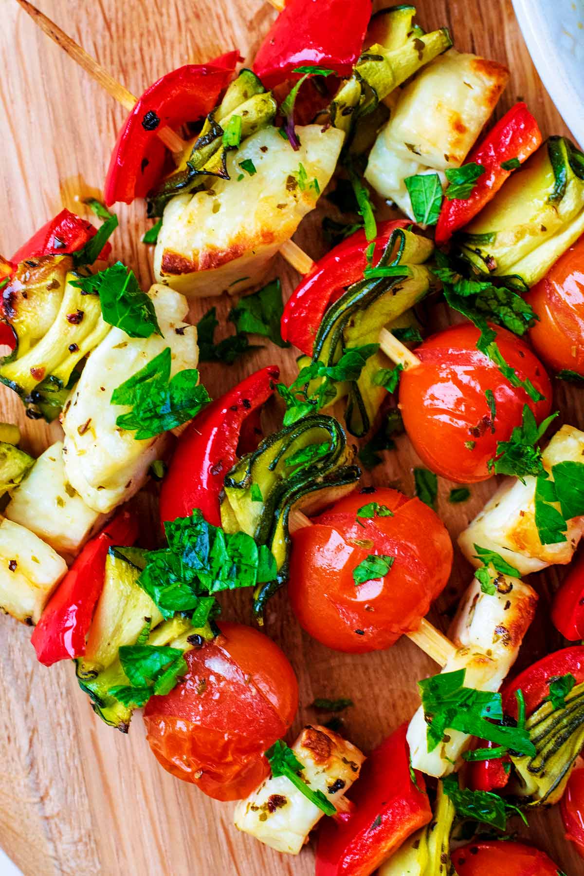 Cooked vegetables and cubes of halloumi on wooden skewers.