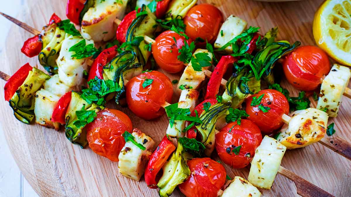 Veg and halloumi skewers on a wooden serving board.