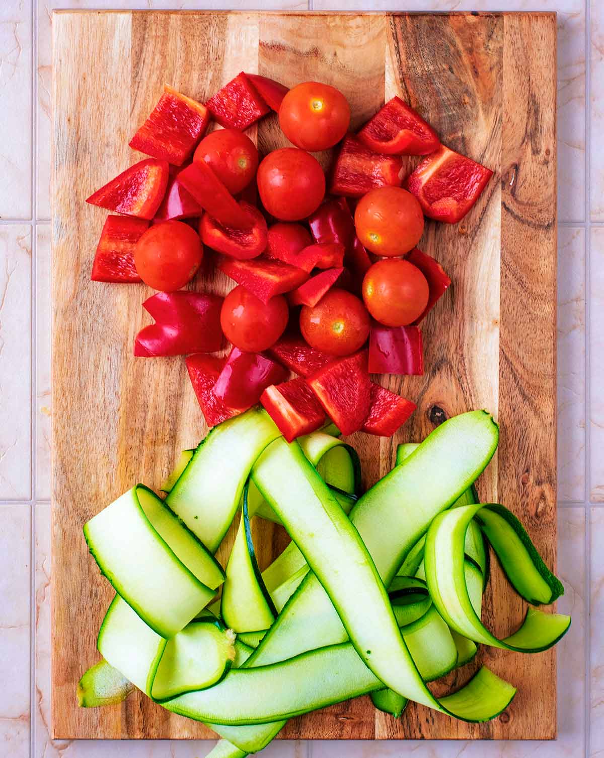 Ribboned courgette, chopped red bell pepper and cherry tomatoes on a wooden chopping board.