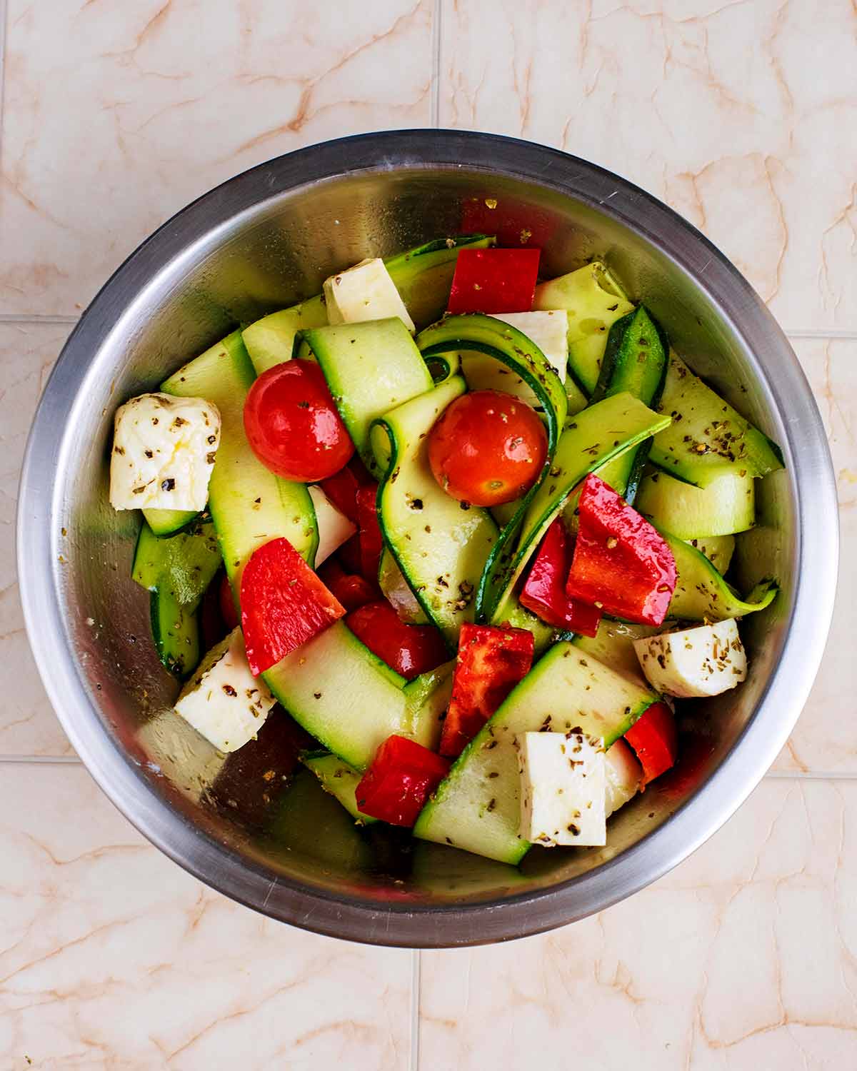 A metal bowl containing chopped vegetables and cubes of halloumi.