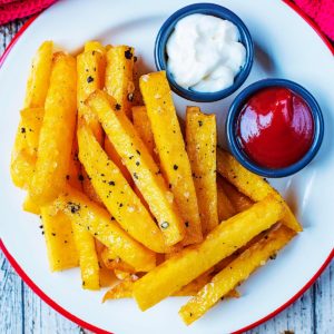 Baked Polenta Fries on a white plate with small pots of ketchup and mayonnaise