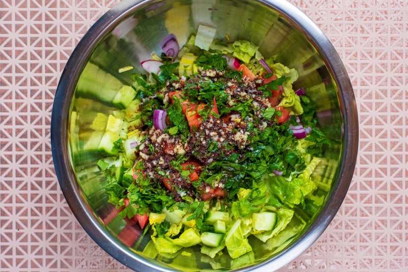 Chopped salad items, herbs and dressing in a large metal mixing bowl.