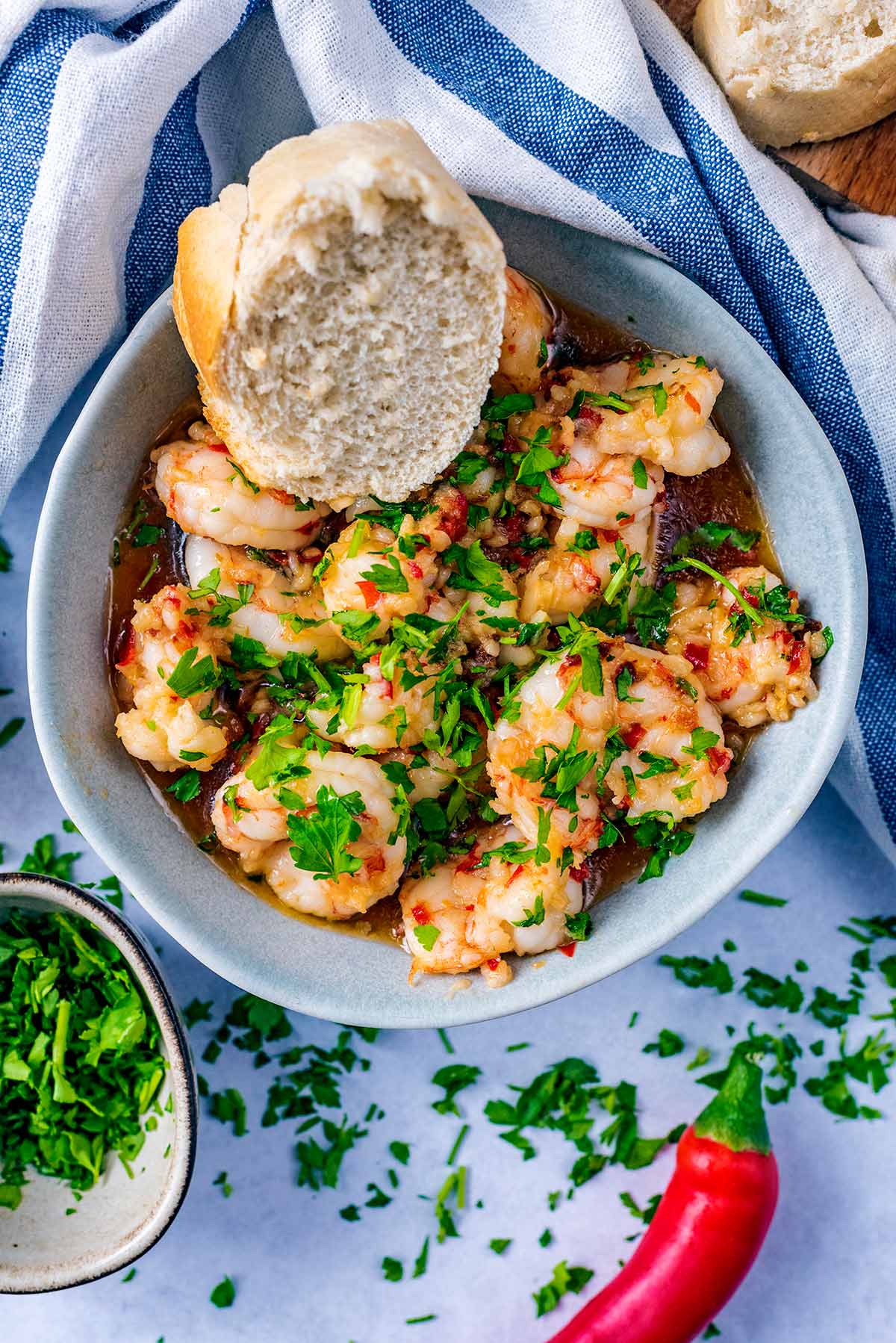 A bowl of cooked prawns, scattered with herbs and a piece of chunky bread.