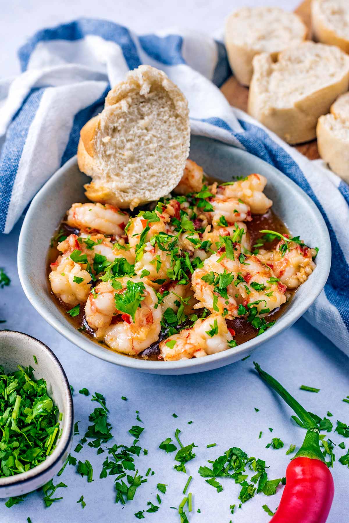 Cooked prawns and a piece of bread in a bowl next to more bread.