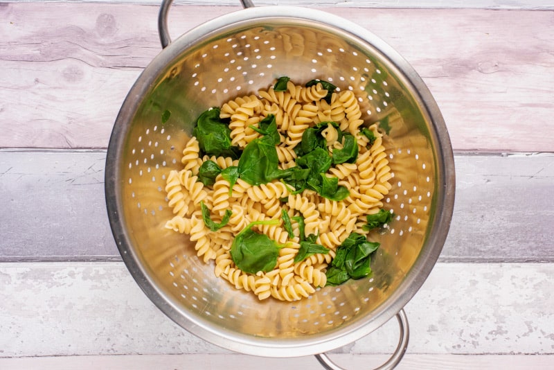 A colander containing drained cooked pasta and spinach.