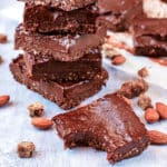 No Bake Brownies stacked up surrounded by almonds and chopped dates.