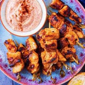 Paprika Chicken Skewers on a plate with paprika dip. Toasted slices of bread are next to the plate