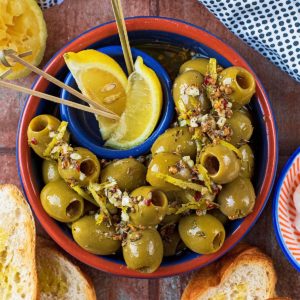 A bowl of green Spanish olives with lemon wedges, Bread and dip are next to it