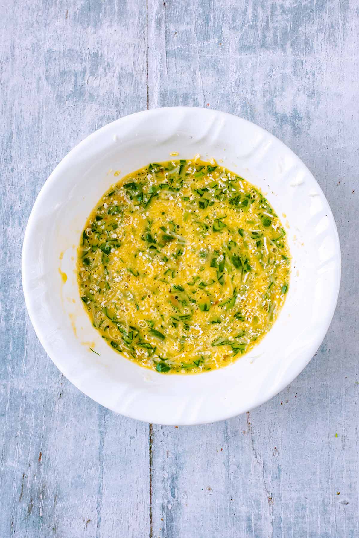 A bowl containing whisked egg, milk, cheese and spinach.