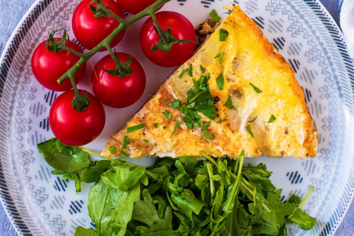 A slice of spanish omelette tortilla with salad and cherry tomatoes.