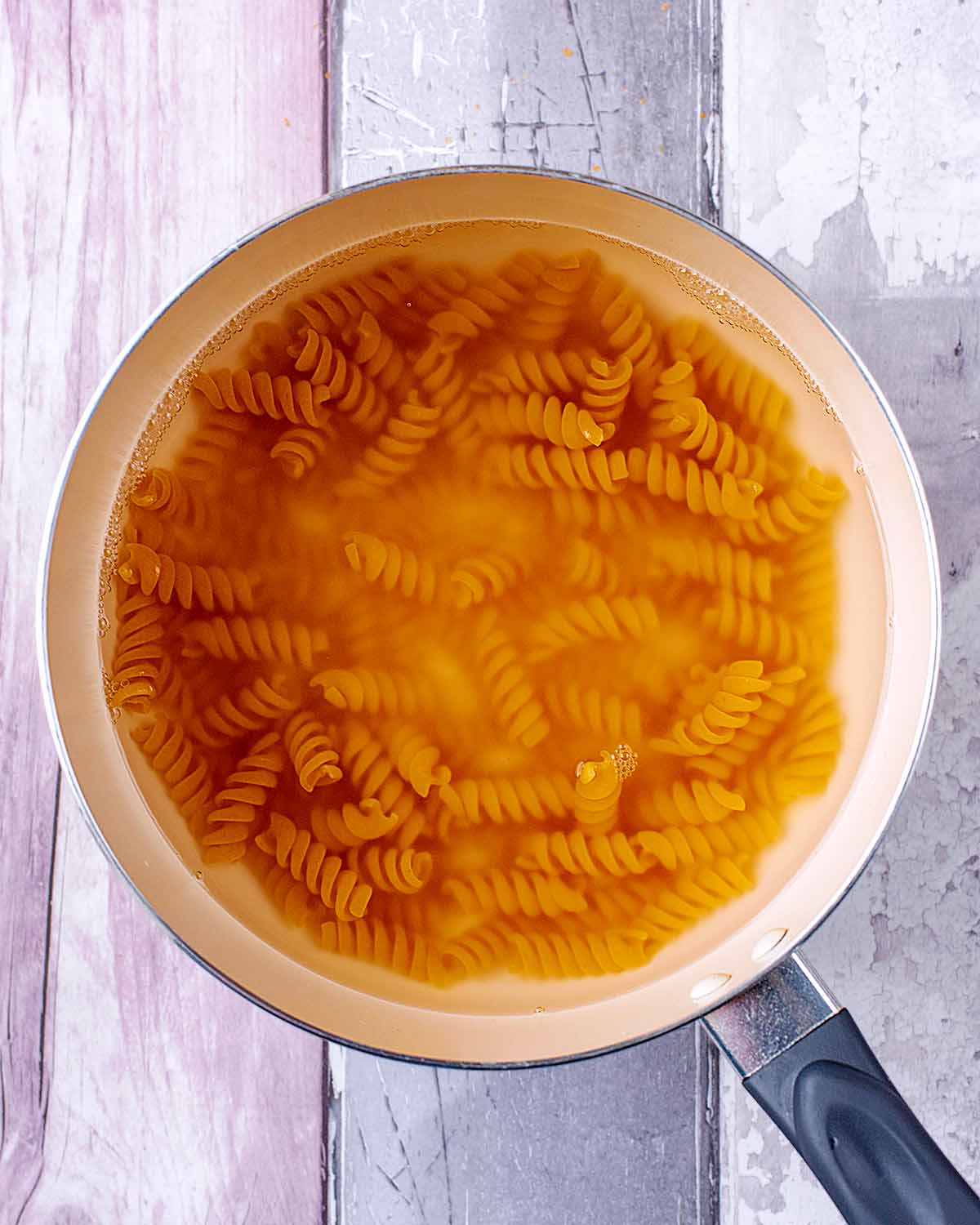 A saucepan containing cooked fusilli pasta in water.