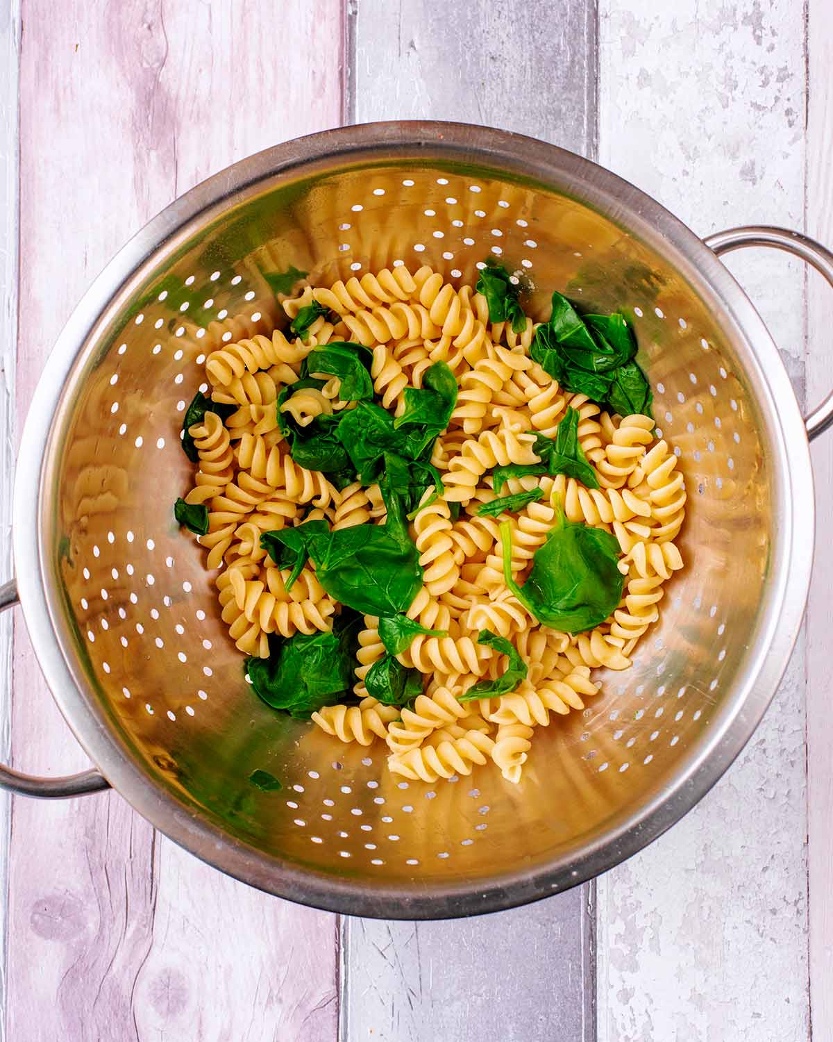 A colander containing drained cooked pasta and spinach.