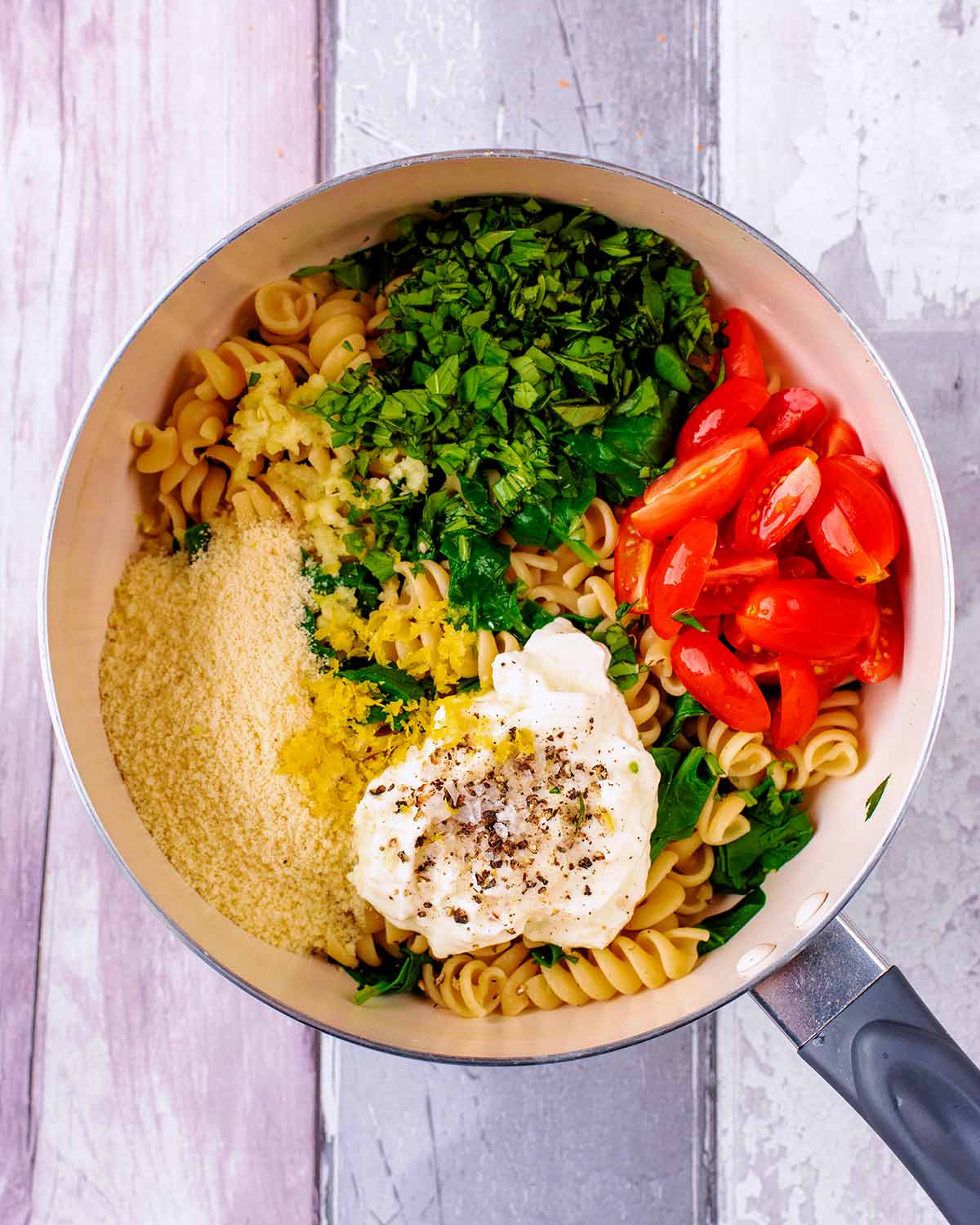 A saucepan containing cooked pasta, chopped spinach, chopped tomatoes, yogurt, cheese and seasoning.