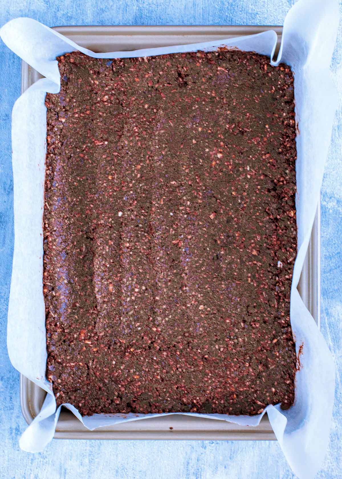 A lined brownie tin with a chocolate crumb base pressed into it.