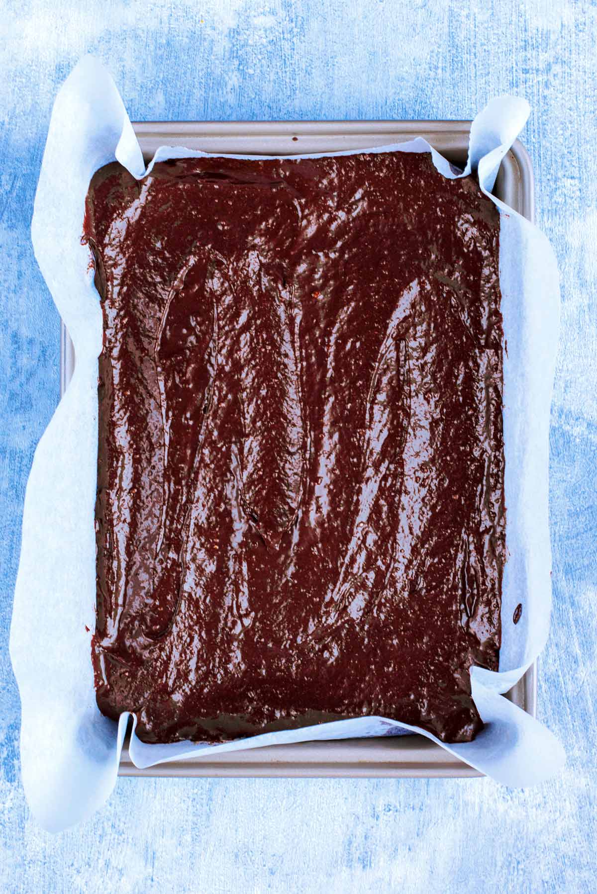 A lined brownie tray with chocolate brownie mix.