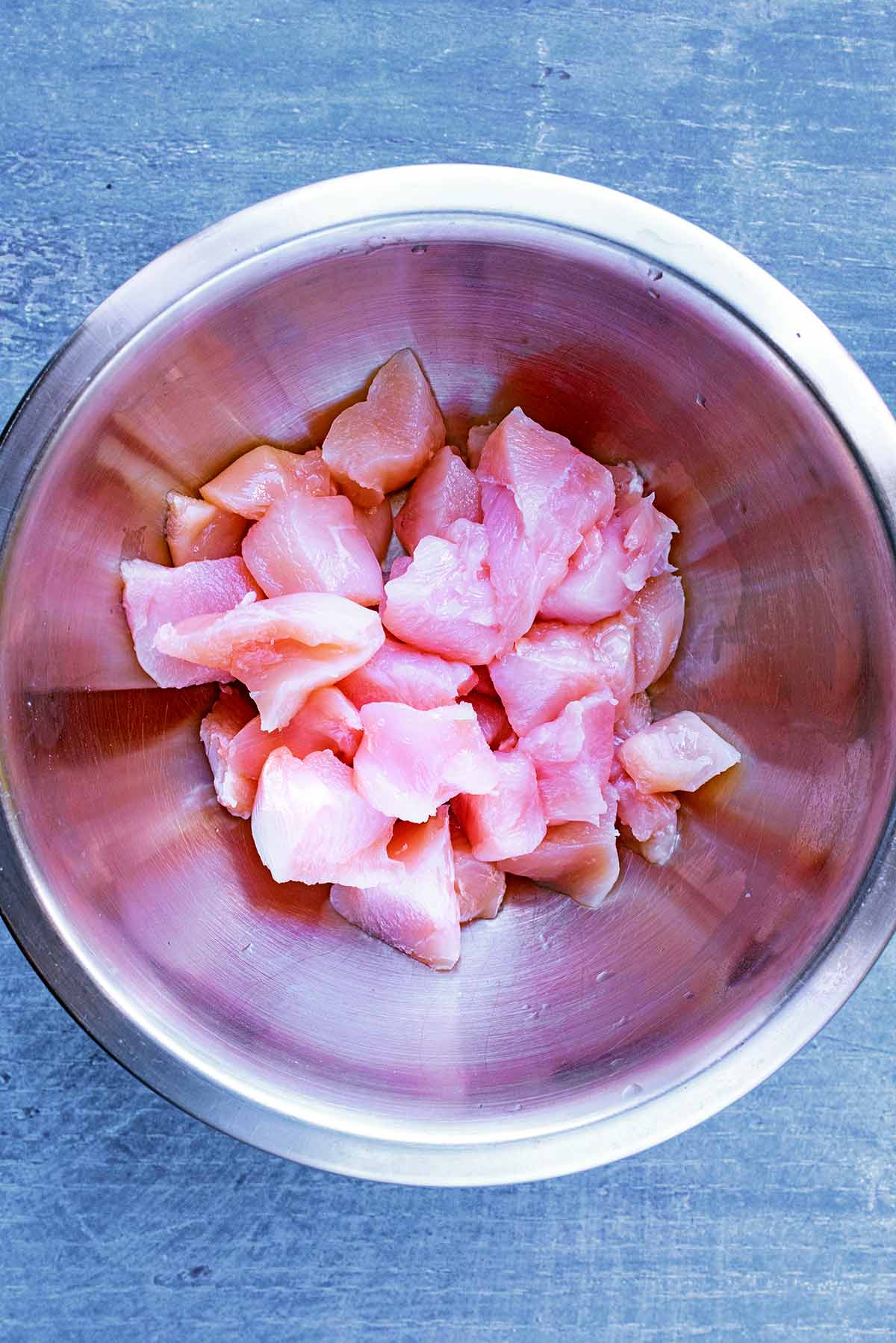Chunks of raw chicken breast in a metal mixing bowl.
