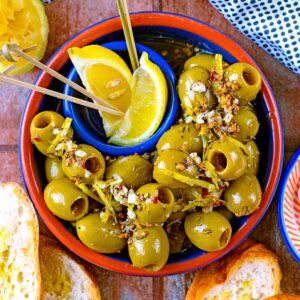 A bowl of green Spanish olives with lemon wedges.