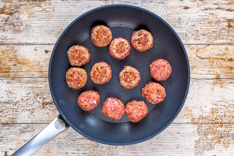 12 meatballs cooking in a black frying pan.