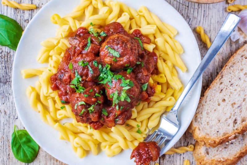 A plate of pasta and meatballs in a tomato sauce topped with chopped herbs.