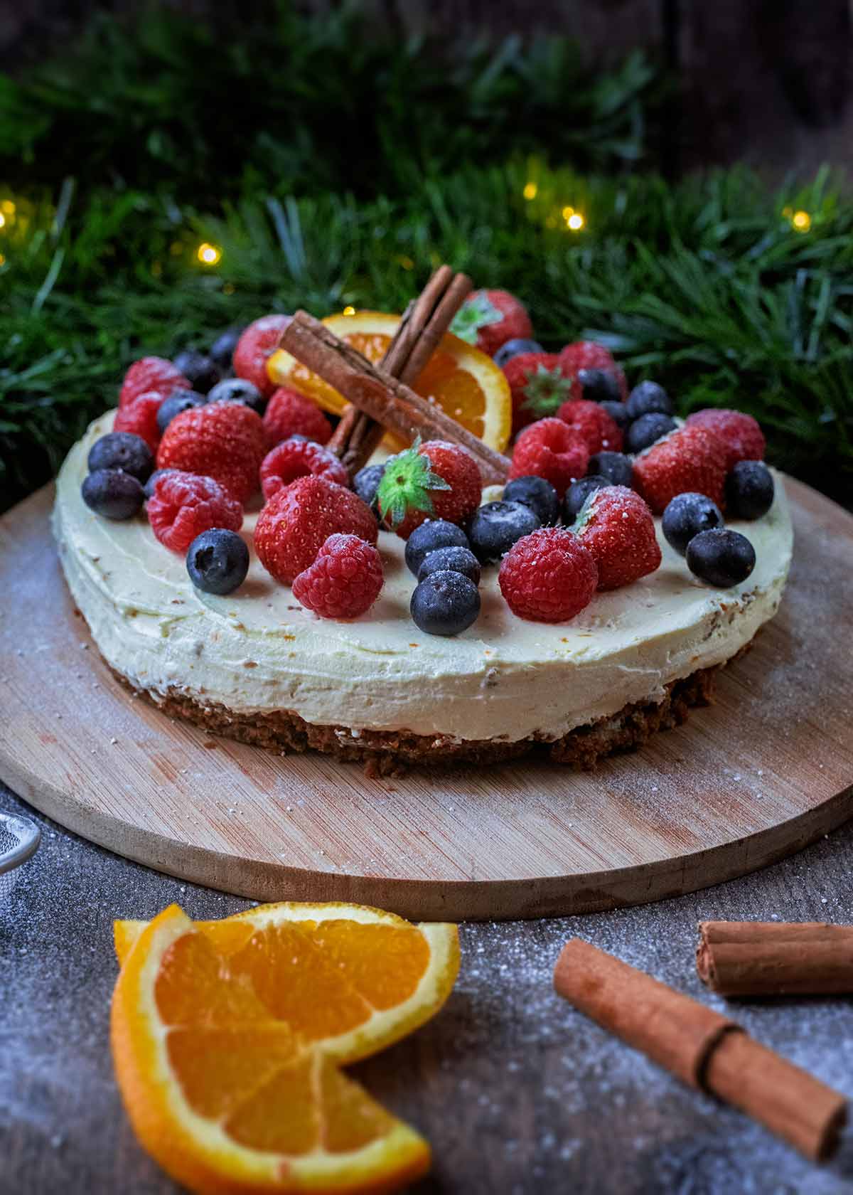 A decorated cheesecake on a wooden board in front of a green festive garland.