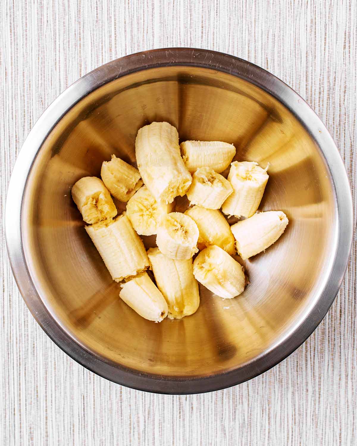 A metal bowl with broken bananas in it.
