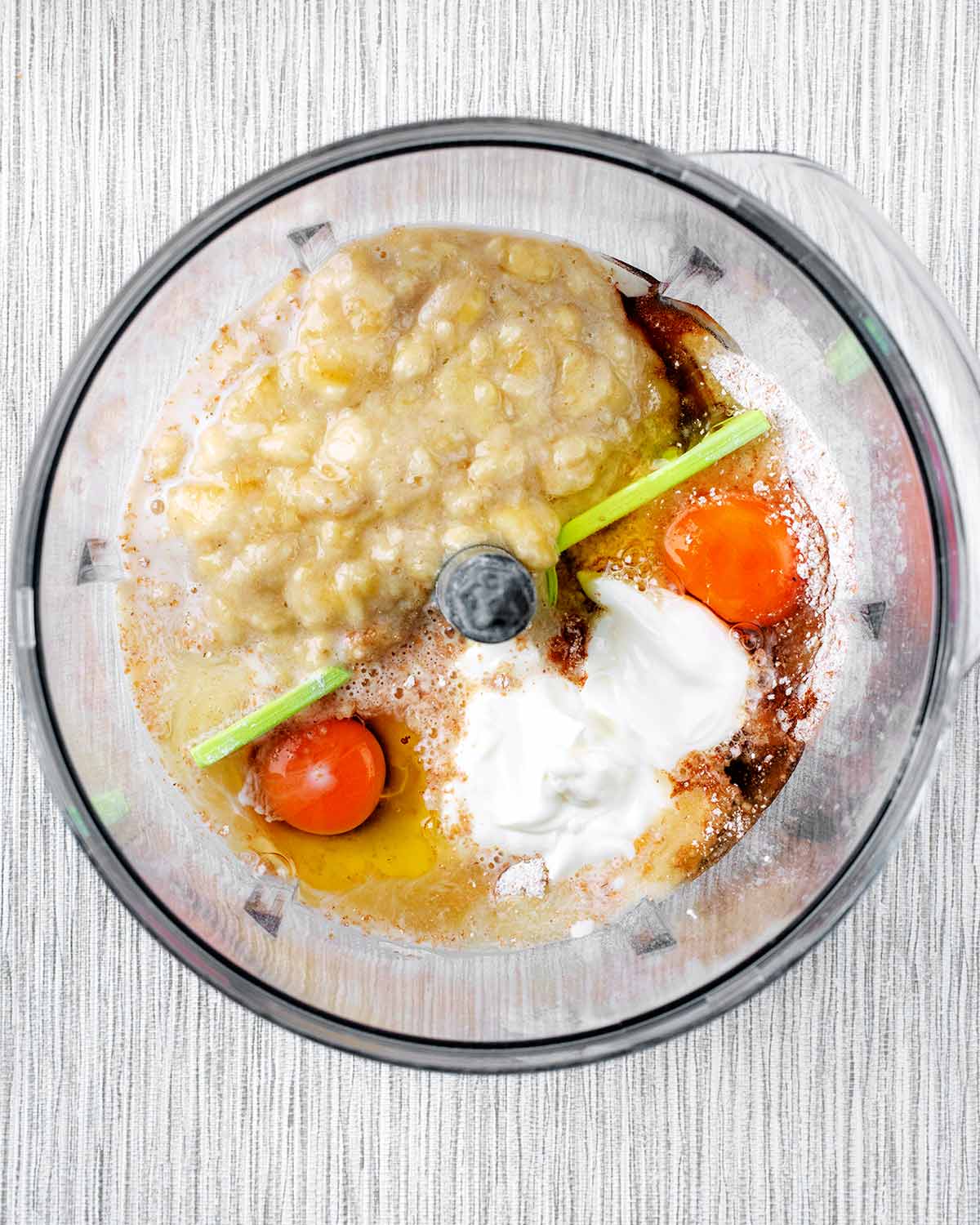 A food processor containing mashed banana, eggs, milk and yogurt.
