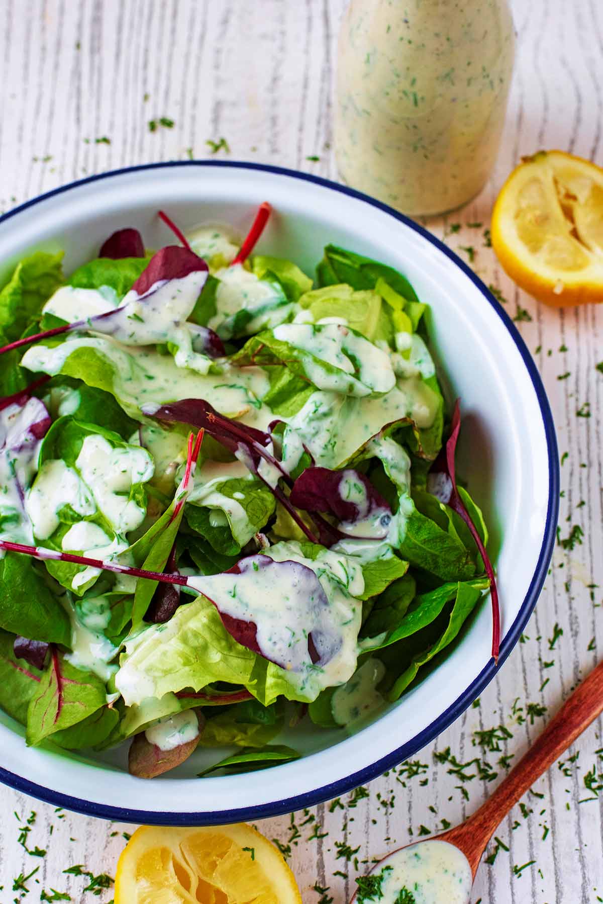 Salad dressing over lettuce next to a sauce bottle and a spoon.