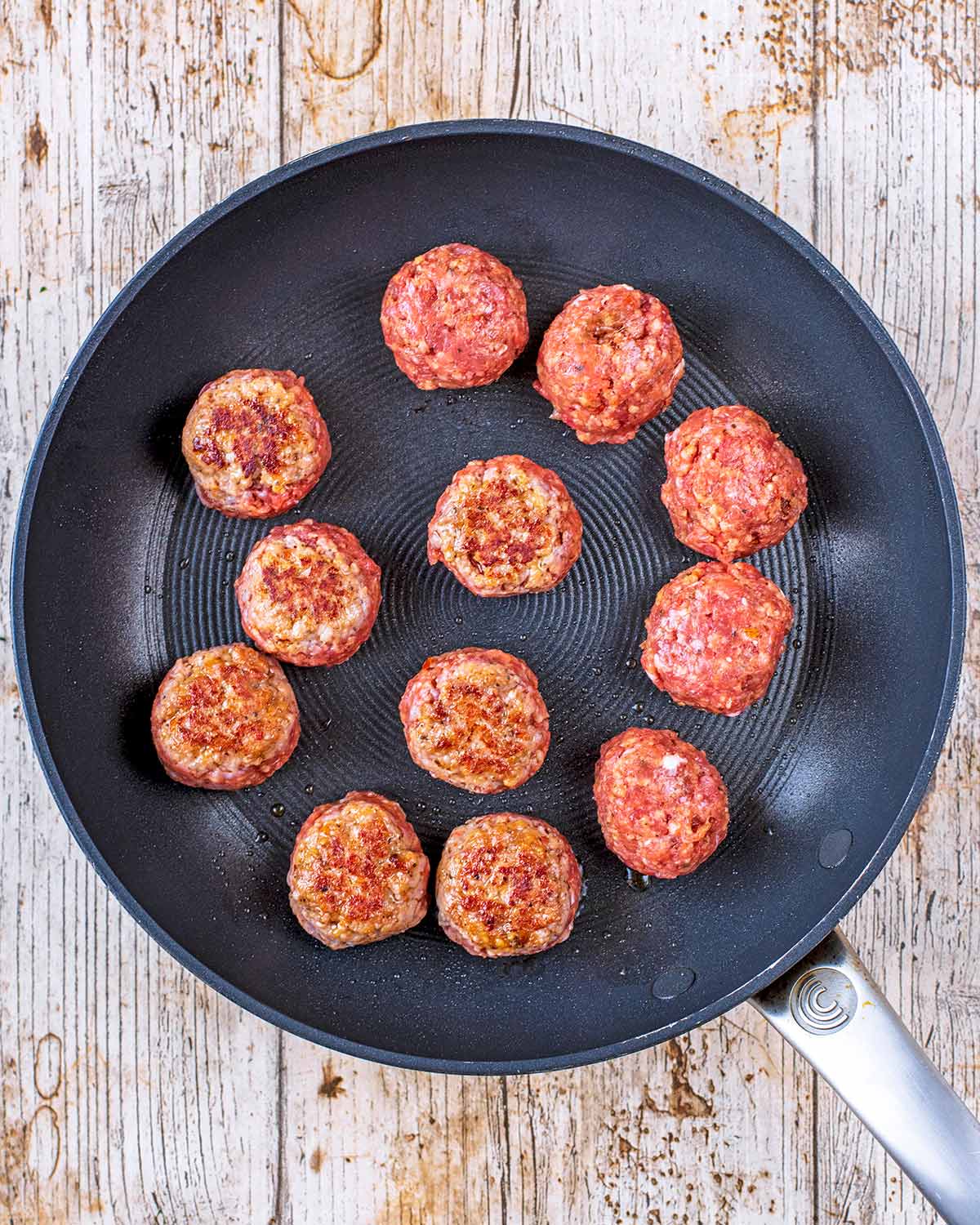 12 meatballs cooking in a black frying pan.