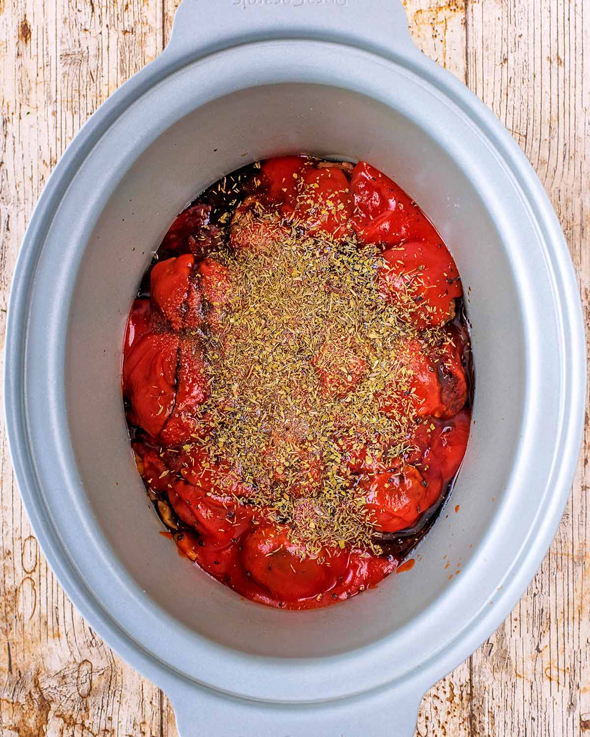 Meatballs in a crock pot covered in tomatoes and herbs.