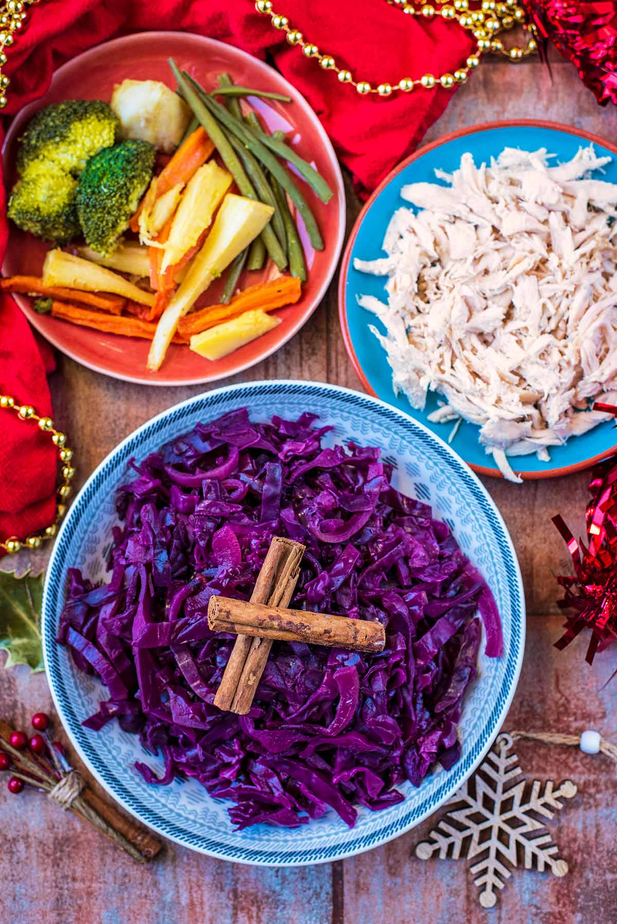 A bowl of cooked red cabbage next to some shredded turkey and some roast vegetables.