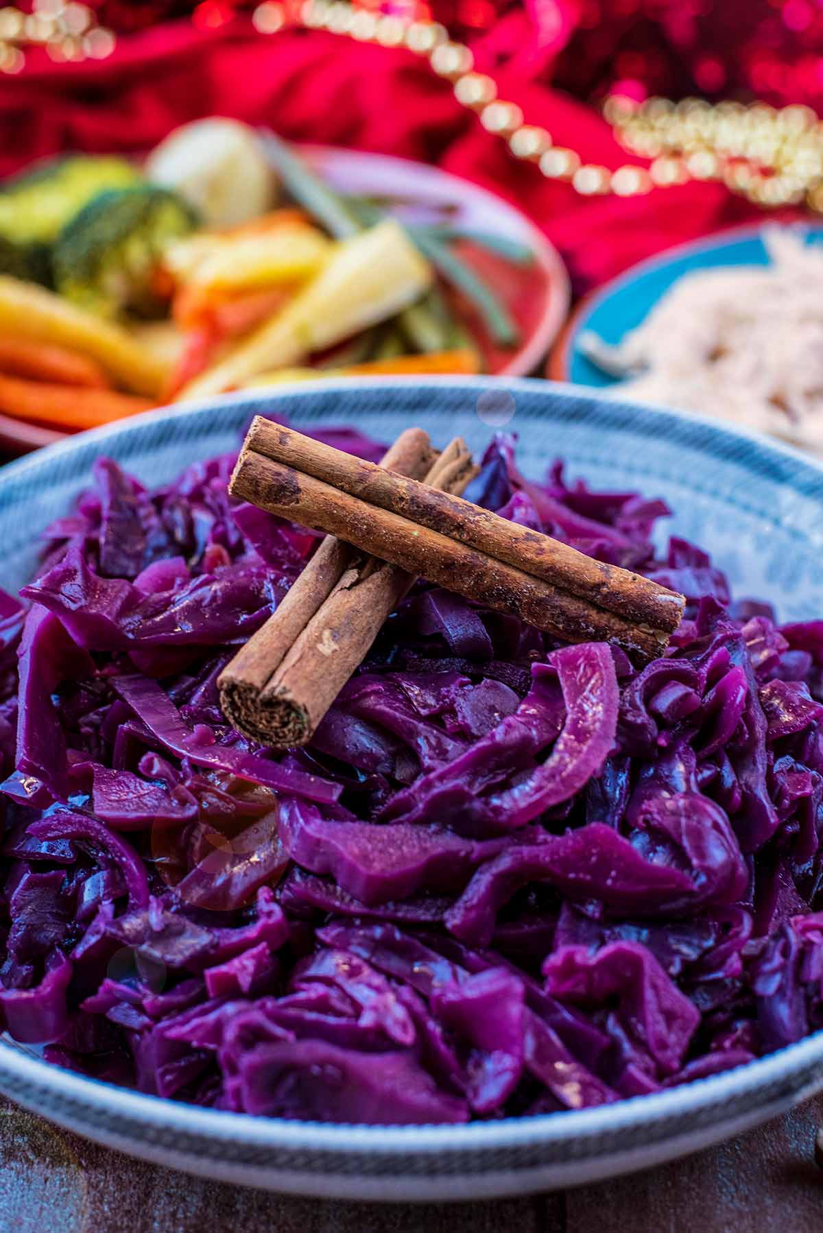 Cooked red cabbage in a large patterned bowl with cinnamon sticks on top.