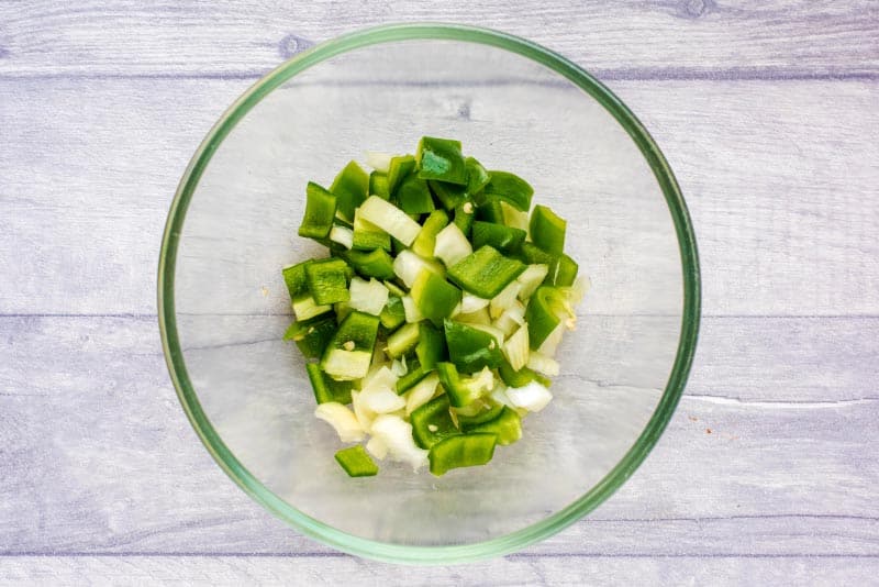 A glass bowl containing chopped onion and green bell pepper.