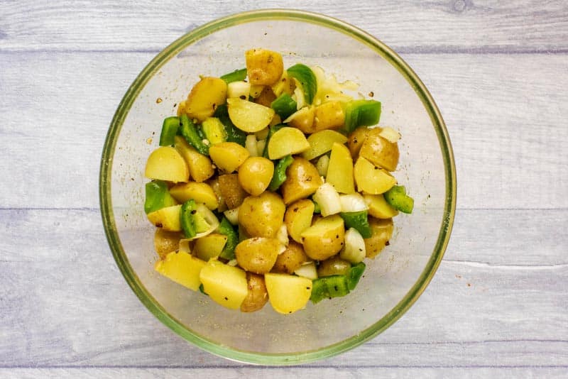 A glass bowl containing cooked cubed potatoes, chopped onion and green bell pepper.