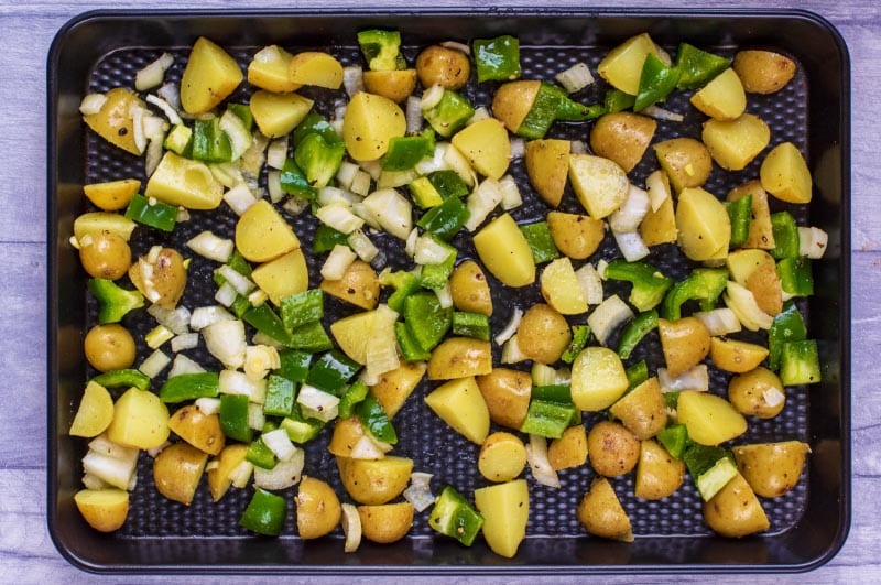 A baking tray covered in cubed potatoes, chopped onions and green bell pepper.