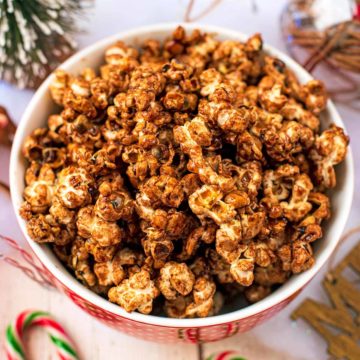 A bowl of Christmas popcorn surrounded by Christmas decorations.