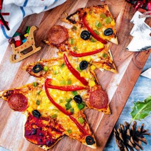A Christmas Tree Pizza on a wooden board with Christmas decorations surrounding it.