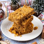 Four cinnamon flapjacks piled on a plate with Christmas decorations in the background.