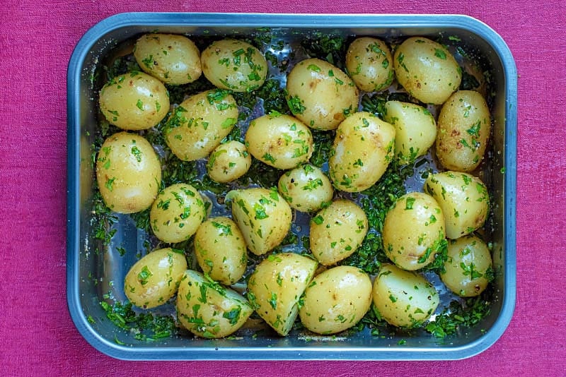 A roasting tin full of halved baby potatoes and herbs.