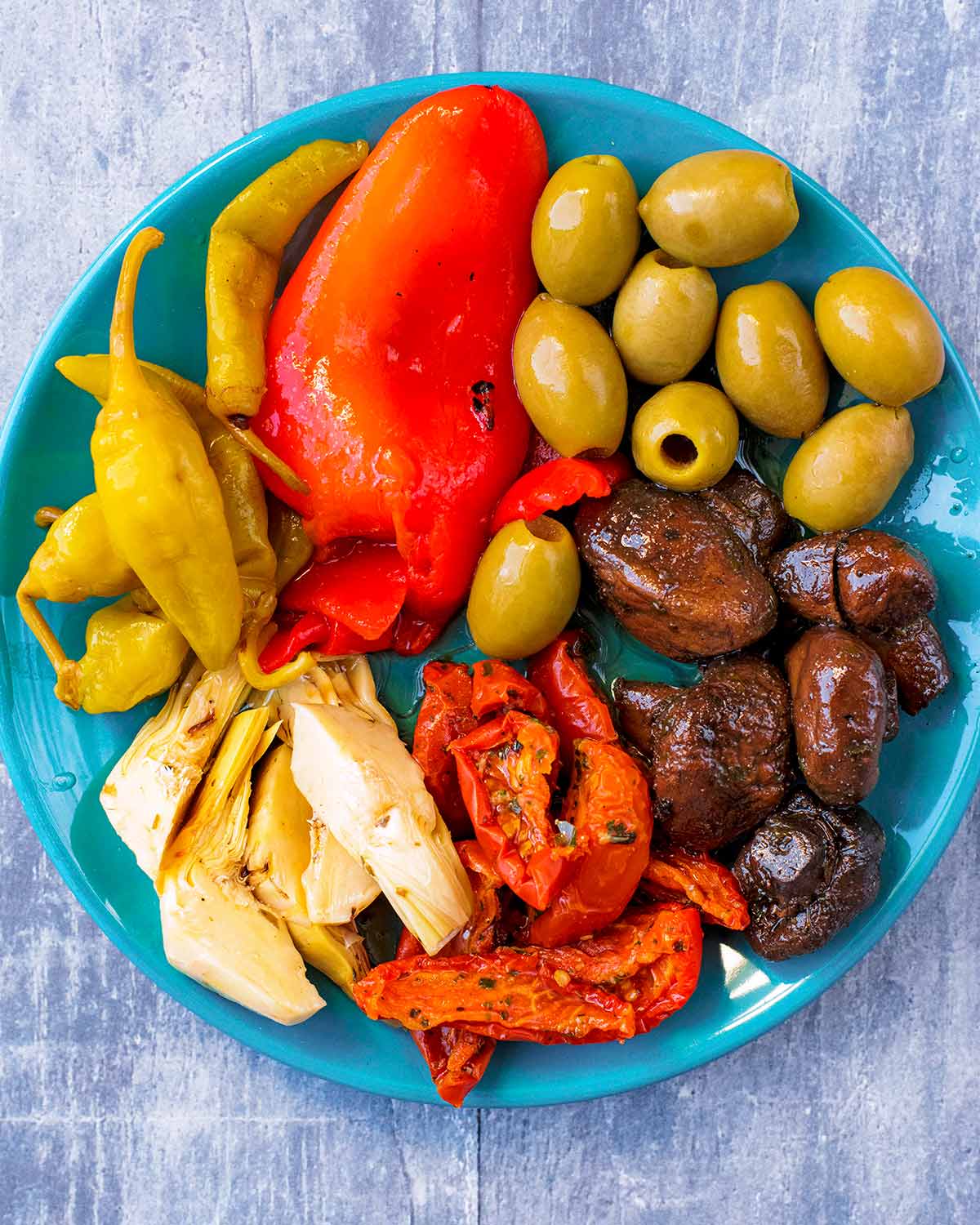 Olives, peppers, mushrooms, artichokes and chillis arranged on a blue plate.